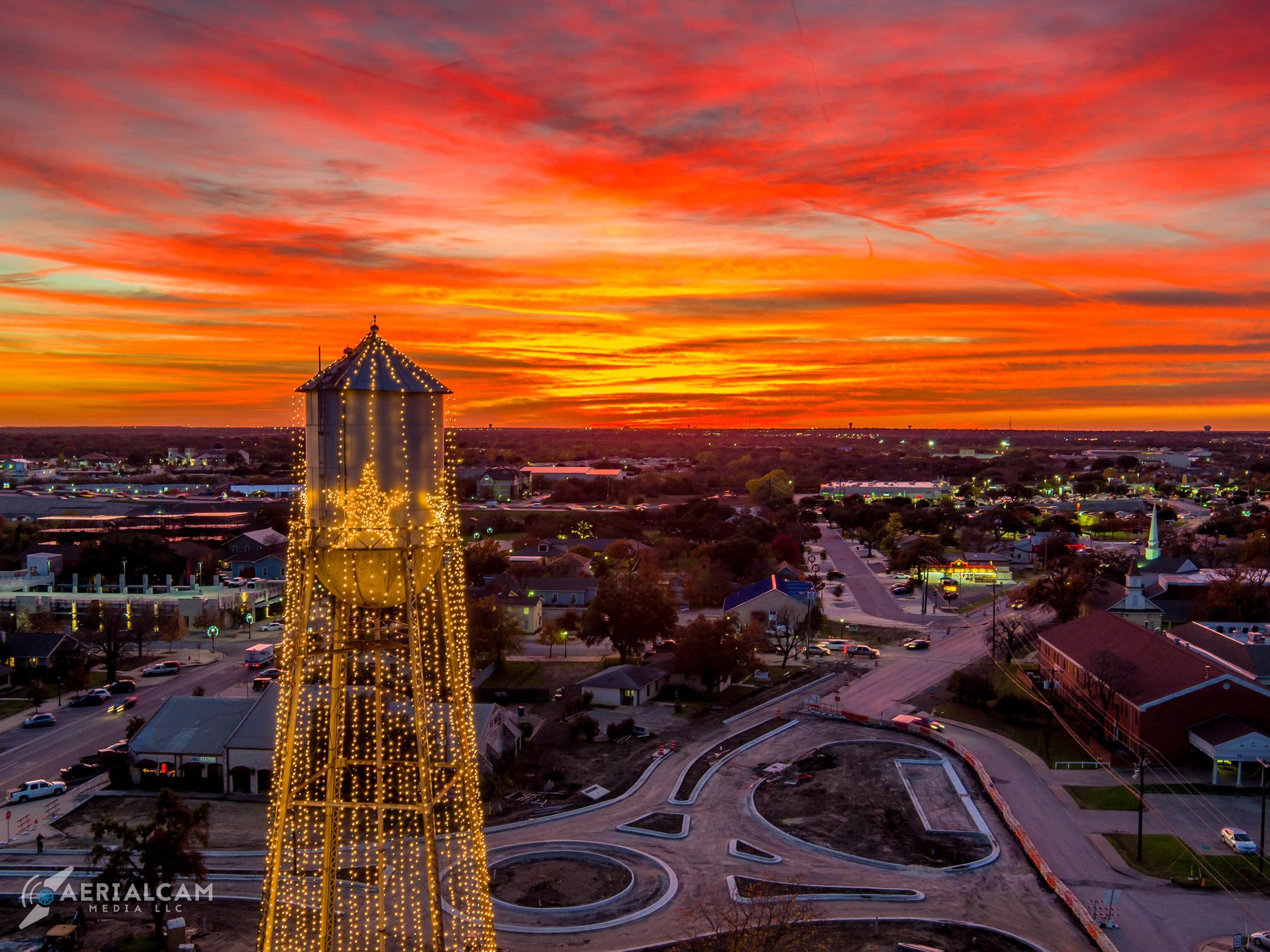 Aerial over a small South Texas town at sunset, lit water tower in the foreground